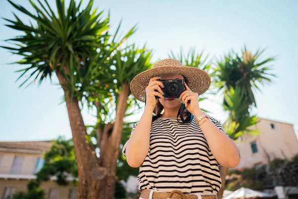 Turistka fotografka stojící pod palmami ve starém řeckém městě. Koncept letních prázdnin. Dáma zkoumá ostrov. Amatér fotografování s malým digitálním fotoaparátem. — Stock fotografie