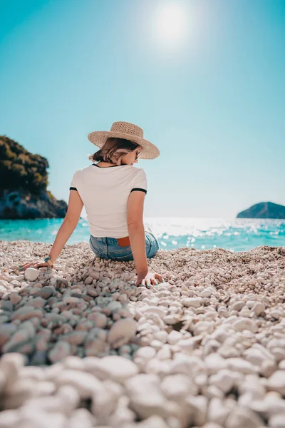 Egy fiatal nő ül a kavicsos parton a Földközi-tenger közelében. Lady turista élvezi nyaralás ideje, néz gyönyörű kék víz felszíni egyedül, természet háttér. — Stock Fotó