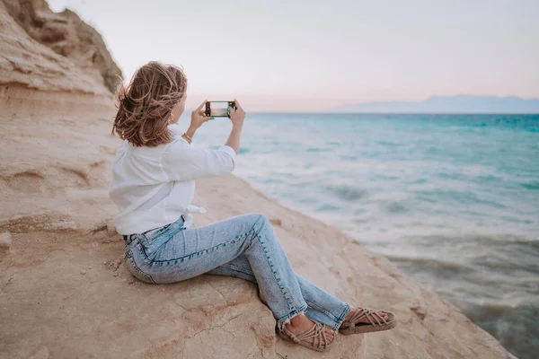 Fiatal nő videózik mobiltelefonnal a tengerparton, közel a kék tengerhez. Lány okostelefon, fotózás a szociális alkalmazás, élvezi a nyaralás ideje. — Stock Fotó