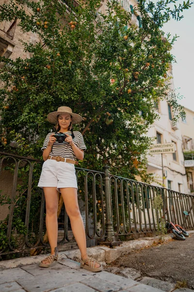Touristenfotografin steht unter einem Granatapfelbaum in der alten griechischen Stadt. Sommerferienkonzept. Lady erkundet Insel. Amateur fotografiert mit kleiner Digitalkamera. — Stockfoto
