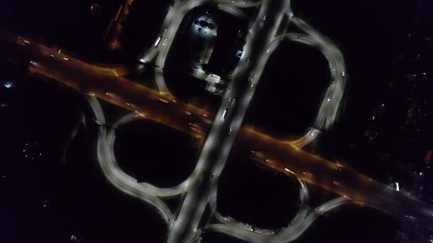Aereo drone vista dall'alto a rotonda corsia, il traffico all'incrocio della città di notte. Auto e camion che guidano su un'autostrada a più livelli. Trasporti, concetto di sviluppo delle infrastrutture. — Video Stock