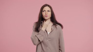 Genç ve güzel bir kadının yarası var. Pembe Stüdyoda Boğazı Şişmiş Hasta Kadın. Anjin. Genç kız acı hissediyor, acı çekiyor. Mevsimsel grip, soğuk algınlığı. Yüksek kalite 4k