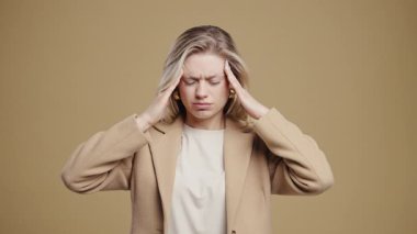 Baş ağrısı, kan basıncı, stüdyo fotoğrafı olan genç bir kadın. Kız ellerini başının üstüne koyuyor, bej arka planda izole edilmiş. Sorun kavramı, ilaç, hastalık. Yüksek kalite 4k