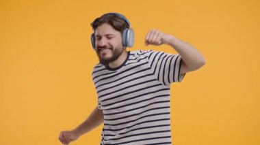 Olgun beyaz adam müzik dinliyor, sarı stüdyo arka planında kulaklıklarla dans ediyor. Radyo, kablosuz modern ses teknolojisi, çevrimiçi çalar. Yüksek kalite 4k