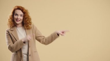 Gülümseyen 30 'lu yaşlardaki bayan reklam için boş bir yer arıyor. Önerilen kadın sol tarafı işaret ediyor, kopyala alanı. Kadın, bej arka planda izole edilmiş bir şey sunuyor. Yüksek kalite