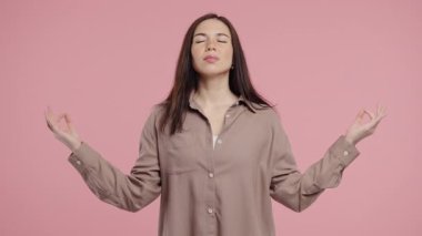 Sakin bir kadın dinleniyor, meditasyon yapıyor, stresi reddediyor. Kadın derin nefes alıyor, sakinleşiyor, pembe stüdyo arka planı. Yoga, ahlaki denge, zen konsepti. Yüksek kalite 4k