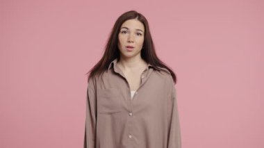 30 'lu yaşlarda güzel bir kadın. Omuzları yukarıda. Yardımcı olamıyor. Zor soru, pembe arka planda suçlu tepkisi. Yüksek kalite 4k