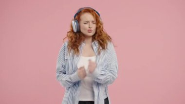 Müzik dinleyen Amerikalı bir kadın, pembe stüdyo arka planında kulaklıkla dans etmekten zevk alıyor. Radyo, kablosuz modern ses teknolojisi, çevrimiçi çalar. Yüksek kalite 4k
