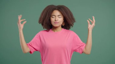 Sakin Afrikalı kadın rahatlıyor, meditasyon yapıyor, stresi reddediyor. Kadın derin nefes alıyor, sakinleşiyor, yeşil stüdyo arka planı. Yoga, ahlaki denge, zen konsepti. Yüksek kalite 4k