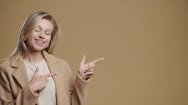 Gülümseyen 30 'lu yaşlardaki iş kadını reklam için boş bir yer arıyor. Önerilen kadın sol tarafı işaret ediyor, kopyala alanı. Kadın, bej arka planda izole edilmiş bir şey sunuyor. Yüksek kalite 4k