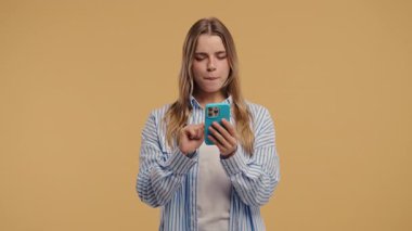 Akıllı telefondan internette sörf yapan güzel bir kadın. Bej arka planda gülücük ve neşe dolu bir kız. Teknoloji, başarı, mutluluk, sosyal ağ konsepti. Yüksek kalite 4k