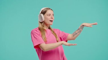 Sarışın kadın müzik dinliyor, mavi stüdyo arka planında kulaklıklarla dans ediyor. Radyo, kablosuz modern ses teknolojisi, çevrimiçi çalar. Yüksek kalite 4k