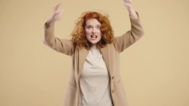 Stres ve öfke içinde bir kadın, saldırganlıkla tehdit ediyor, bağırıyor ve bej rengi kameraya bakıyor. Öfkeli kızıl saçlı Amerikalı kadın. Çatışma, tartışma, stres, duygusal patlamalar. Yüksek kalite 4k görüntü