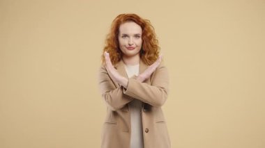 Onaylamayan ciddi bir kızıl kadın bej renkli stüdyo arkaplanında reddetme işareti yapıyor. Ban, mola. Yüksek kalite 4k görüntü