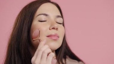 Rose Quartz 'ın Taş Roller' ı ile Yüze Masaj Yapan Genç Kadın, Sert, Yumuşak Cilt İçin. Yüz bakımı, gerçek vücut, çeşitlilik, kapsayıcı, otantik. Yüksek kalite 4k