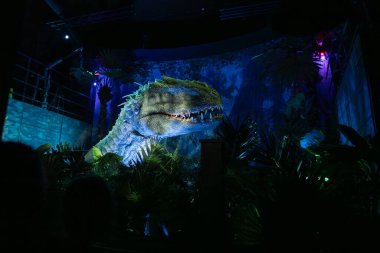 Madrid, İspanya - 18.12.2025. Jurassic World - Tecrübe Sergisi. Devasa Indominus Rex figürü. Dinozor çok renkli ışık, sinematik atmosfer ile aydınlatılır. Eğlence, pop kültürü.