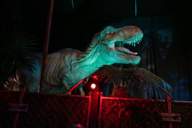 Madrid, İspanya - 18.12.2025. Jurassic World - Tecrübe Sergisi. Devasa bir Tyrannosaurus Rex figürü. Dinozor çok renkli ışık, sinematik atmosfer ile aydınlatılır. Eğlence, pop kültürü.