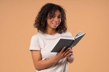 Güzel okuyucu kadın parlak bej arka plana karşı duruyor, elinde tuhaf, meşgul bir ifadeyle kitabı tutuyor ve okuyor. Akıllı kız. Keşif, öğrenme, entellektüel merak, kaliteli zaman geçirme