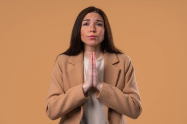 Bej renkli stüdyo arka planında dua eden hoş bir kadın. Güzel bayan birine arzularını tatmin etmesi için yalvarır, yardım eder, şans için dua eder. Yüksek kalite fotoğraf