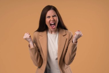 Stres ve öfke içinde bir kadın, saldırganlıkla tehdit ediyor, bağırıyor ve bej rengi kameraya bakıyor. Öfkeli kahverengi saçlı iş kadını. Çatışma, tartışma, stres, duygusal patlamalar. Yüksek kalite fotoğraf