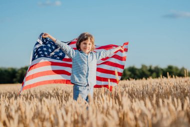 Rüzgarda dalgalanan Amerikan bayrağını sallayan küçük çocuk. ABD derin tarım mirası, vatansever ruh, toprak, yeni nesil. Çiftçilik, kimlik, bağımsızlık. Yüksek kalite fotoğraf