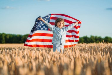 Rüzgarda dalgalanan Amerikan bayrağını sallayan küçük çocuk. ABD derin tarım mirası, vatansever ruh, toprak, yeni nesil. Çiftçilik, kimlik, bağımsızlık. Yüksek kalite fotoğraf