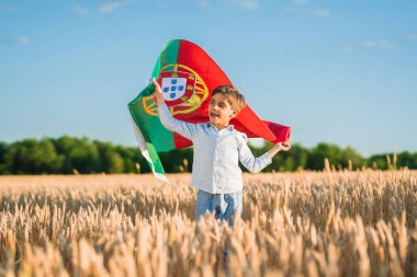 Genç çocuk Portekiz bayrağını rüzgarda sallayarak sahada duruyor. Ulusal gurur, çocukluk hayalleri ve futbol ruhu, Portekiz Günü ve büyük kültürel kutlamalar.