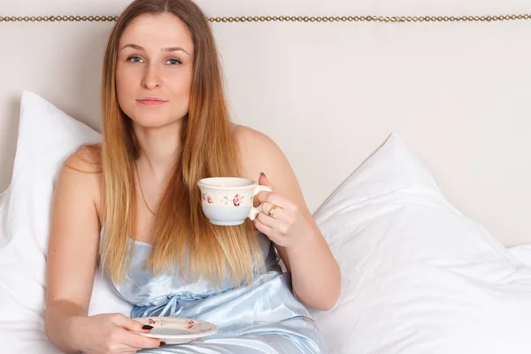 Woman in pajamas holding cup of tea on bed — Stock Photo, Image