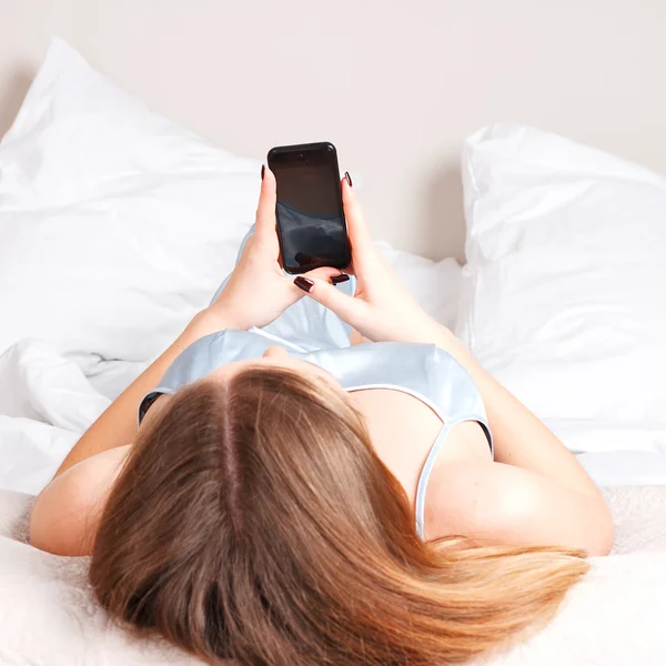 Young woman using smartphone on the bed — Stock Photo, Image