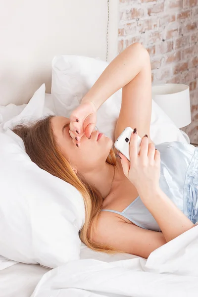 Genç kadın yatakta Smartphone kullanarak — Stok fotoğraf