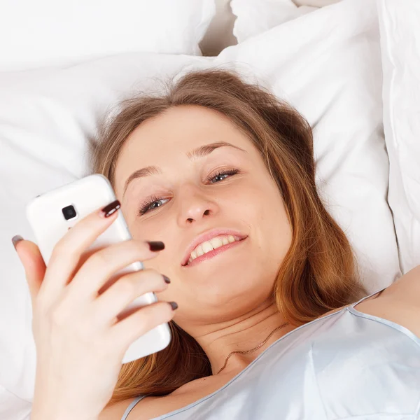 Mladá žena pomocí smartphone na postel — Stock fotografie