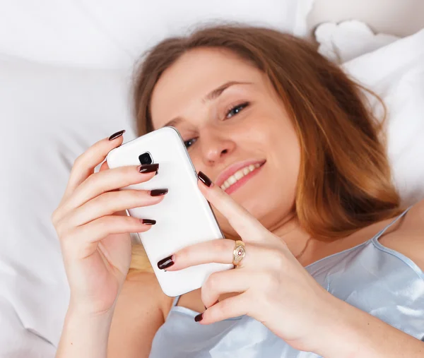 Young woman using smartphone on the bed — Stock Photo, Image