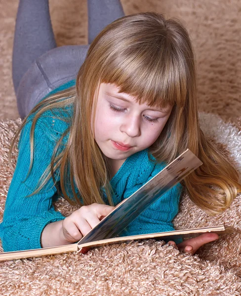 Дівчина читає книгу, лежачи на килимі — стокове фото
