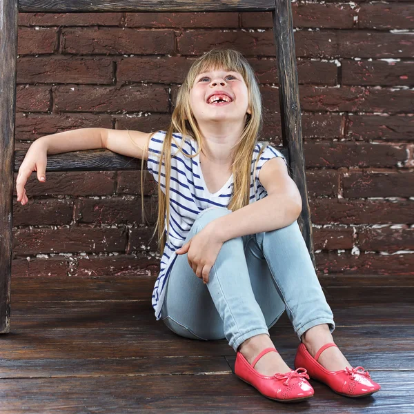 Menina 6 anos de idade em jeans e um colete se senta — Fotografia de Stock