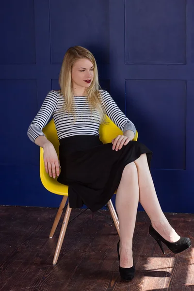 Sarışın kız etek ve yelek bir sandalyede oturur — Stok fotoğraf