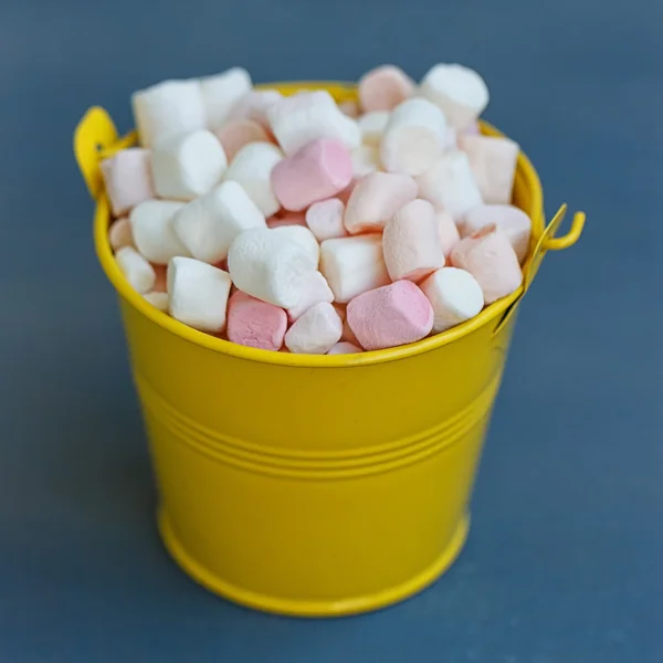 Gele emmer met een marshmallow op blauwe houten achtergrond — Stockfoto