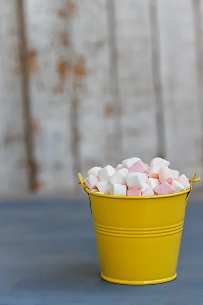 Gele emmer vol met marshmallow passage aan boord tegen witte planken — Stockfoto