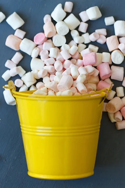 Marshmallow vliegt over de gele emmer op blauwe houten achtergrond — Stockfoto