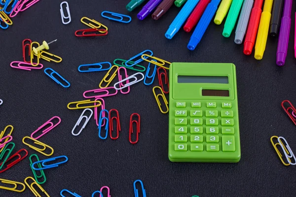 calculator, paper clips, markers on black Board