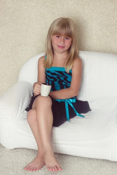 5-jähriges Mädchen sitzt auf einem Sofa mit Tasse — Stockfoto