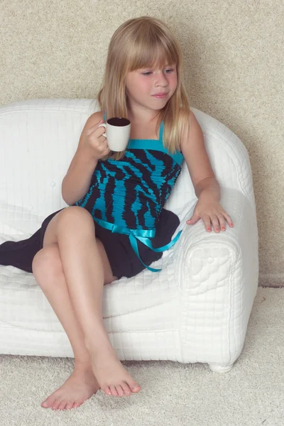 Girl 5 years old sitting on a sofa with cup — Stock Photo, Image