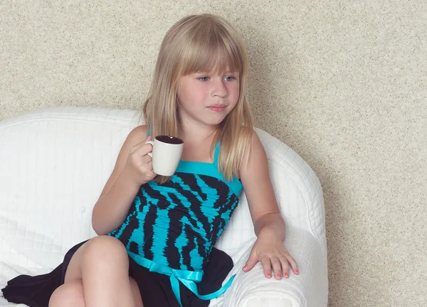 Girl 5 years old sitting on a sofa with cup — Stock Photo, Image