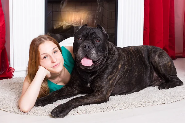 Girl lying near the fireplace with dog Cane Corso — Stock Photo, Image