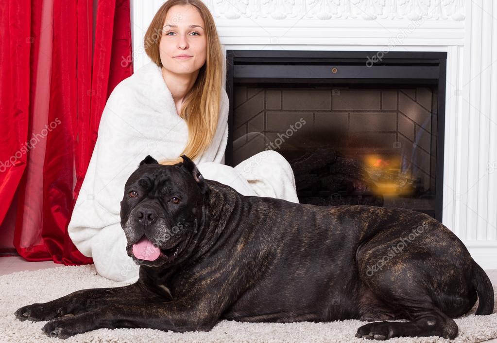 girl wrapped in a blanket sits near the fireplace with dog Cane Corso