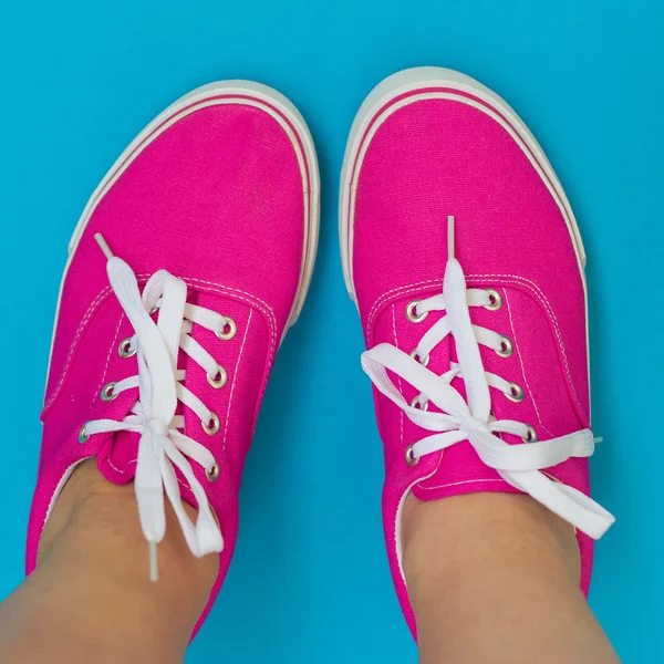 在蓝色背景上的粉红色运动鞋的双腿 — 图库照片