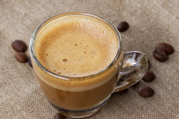 Cappuccino con crema in tazza trasparente sul sacco.con chicchi di caffè chiudi — Foto Stock