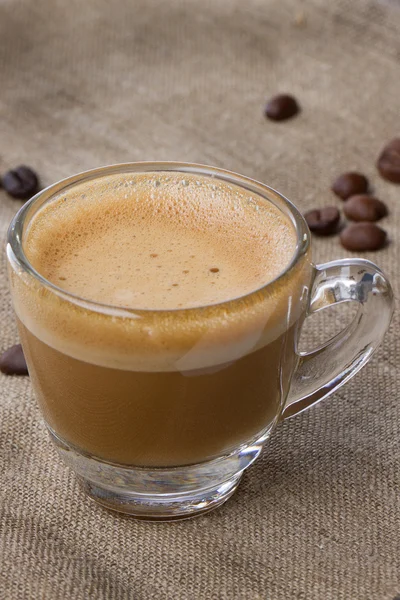 Cappuccino com crema em uma xícara transparente em saquear. grãos de café fechar vertical — Fotografia de Stock