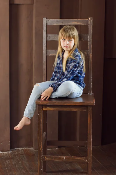 Chica 6 años de edad jeans y una camisa azul está sentado en la silla alta en la habitación —  Fotos de Stock