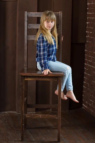 Chica jeans y camisa azul está sentado en una silla alta en la habitación con paredes marrones —  Fotos de Stock