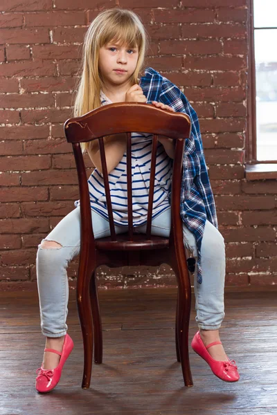 Girl  in jeans and shirt thrown sits on a chair Royalty Free Stock Images